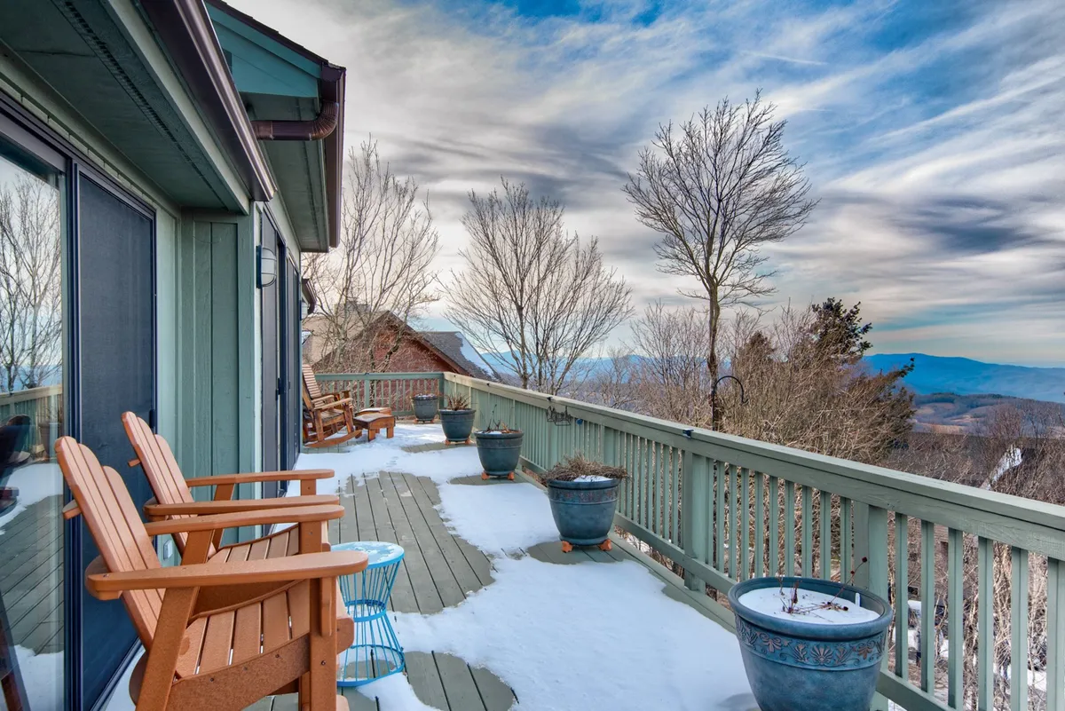This image presents a tranquil exterior deck scene with reclining wooden chairs, colorful plant pots, and a panoramic view of the mountains. While the deck is snow-covered in the image, the openness and layout emphasize the direct connection to nature and the mountains’ scenic beauty, making it a prime spot for leaf peeping during autumn.