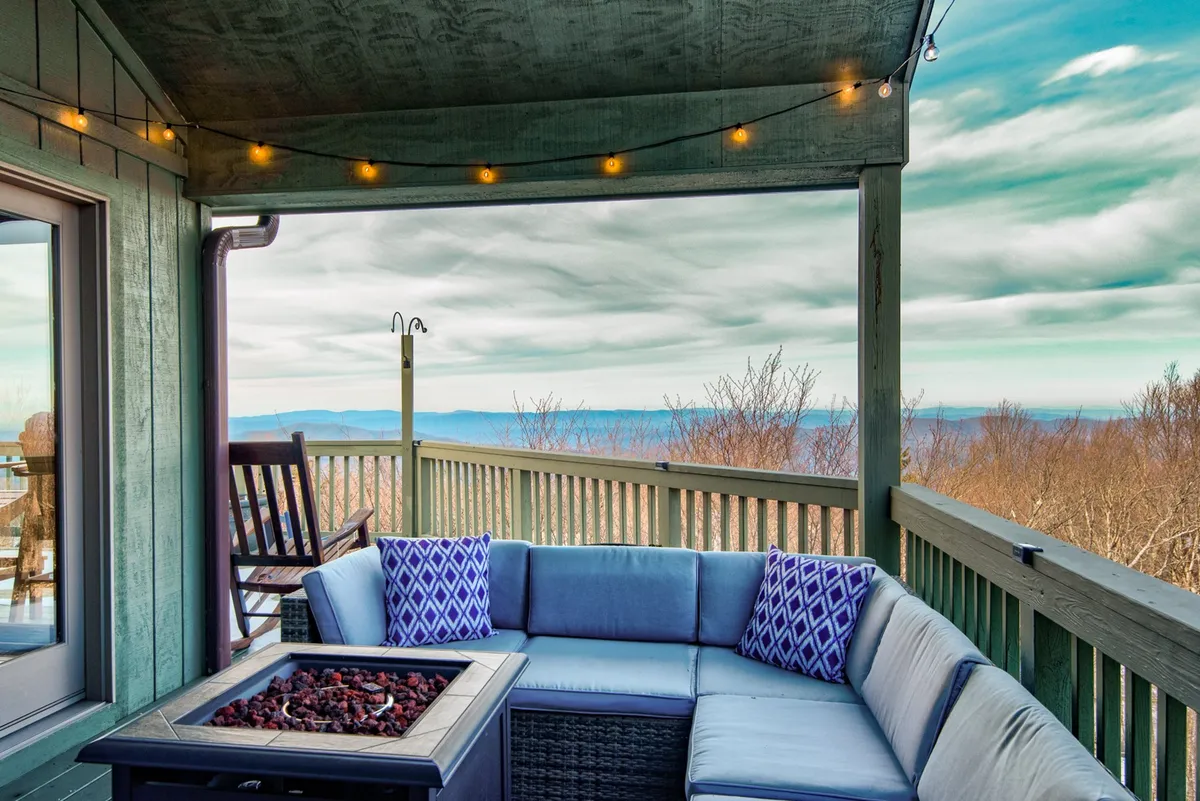 A cozy fire pit surrounded by comfortable outdoor seating, with twinkling string lights overhead and expansive mountain views in the background. The ambiance suggests relaxing evenings and warm gatherings under the stars.