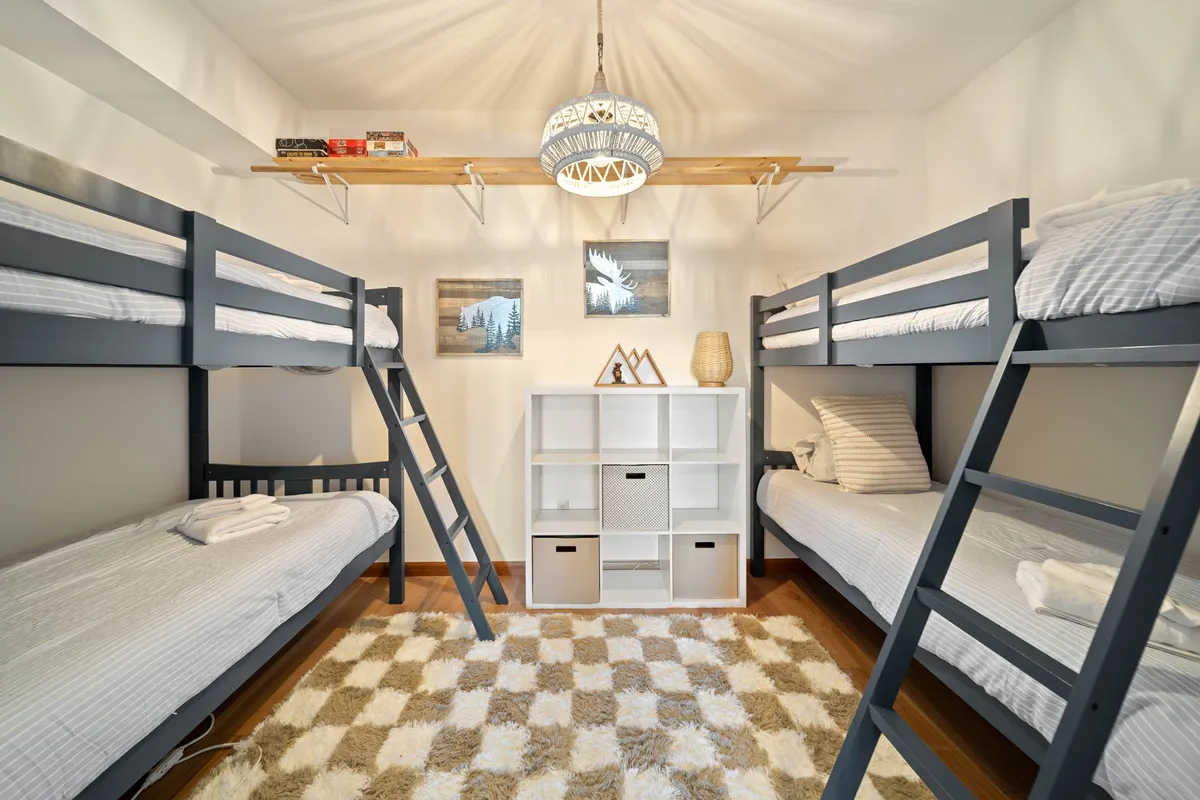 A playful guest bedroom with fun bunk beds, a chandelier, a shelf with books, and a shelving unit, offering a welcoming, family-friendly atmosphere. The space invites relaxation, reading, and playful bonding for kids or groups.