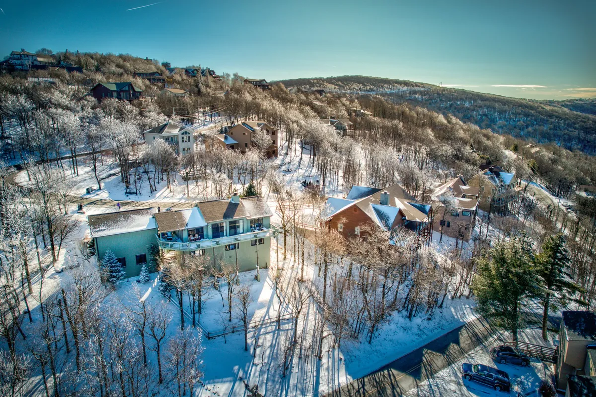 A tranquil winter scene showing several houses nestled amid snow-covered hills and trees. The landscape is blanketed in fresh snow, with gentle slopes ideal for skiing and snowboarding visible in the distance. The atmosphere is serene, evoking the excitement of winter sports and outdoor play.