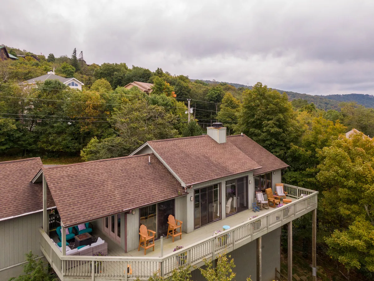 The home’s exterior with inviting deck chairs arranged on the deck, set against a backdrop of trees and greenery. The scene suggests peaceful mornings with coffee or evenings enjoying the fresh mountain air.