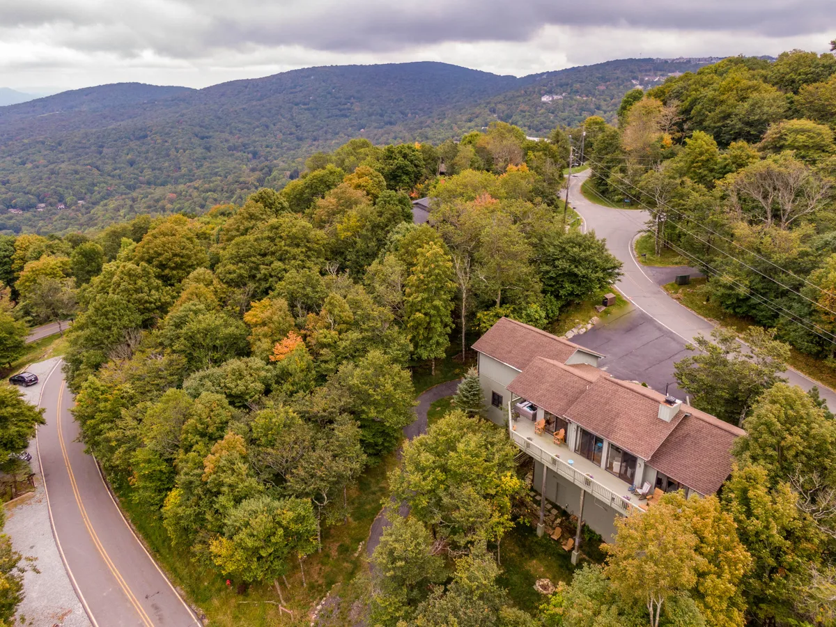 This image shows the house perched on a hillside, embracing the surrounding trees and mountains. The winding road below hints at the adventure that awaits, and the scene conveys a sense of immersion in nature and easy access to outdoor activities.