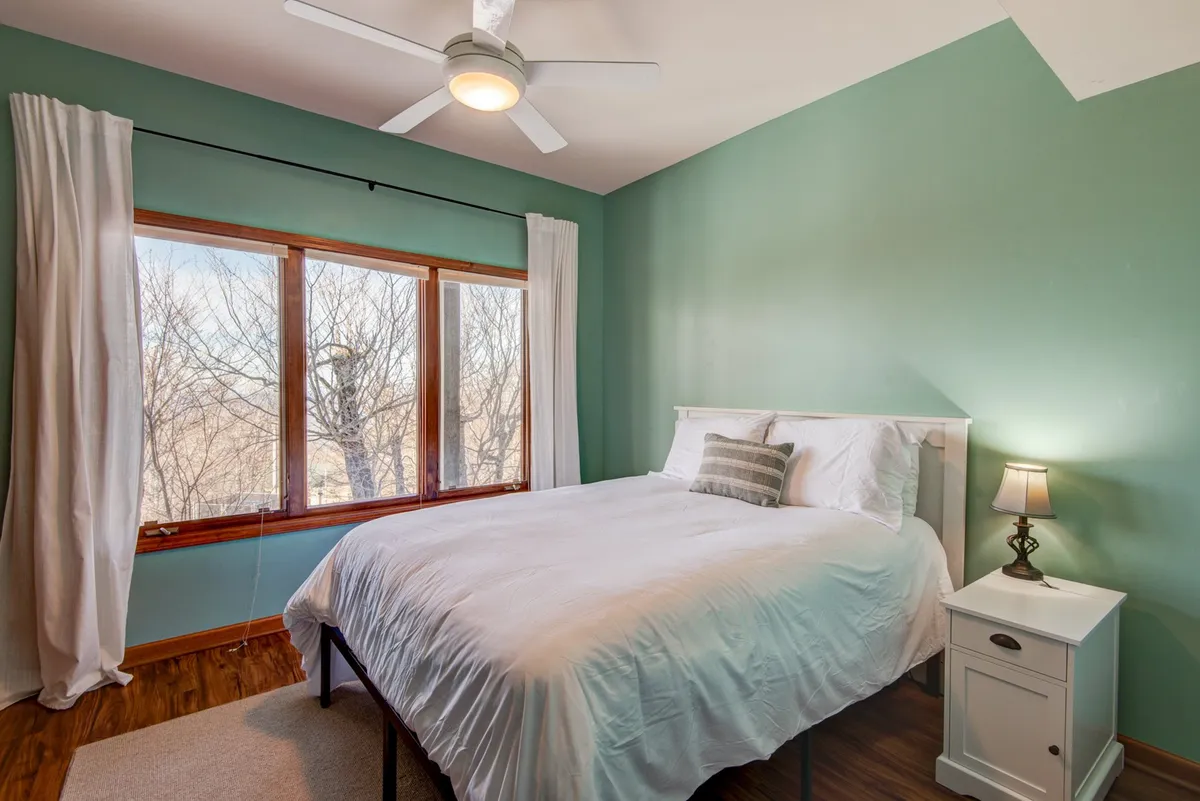 A serene bedroom with crisp white linens on the bed, large windows that let in natural light, and a simple nightstand with a lamp. The view from the windows suggests peace and privacy, reinforcing the quiet, romantic atmosphere described in the section.